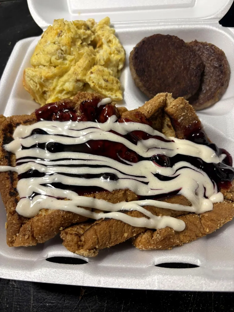 Chicken-fried steak drizzled with cherry topping and icing, served with scrambled eggs and sausage patties
