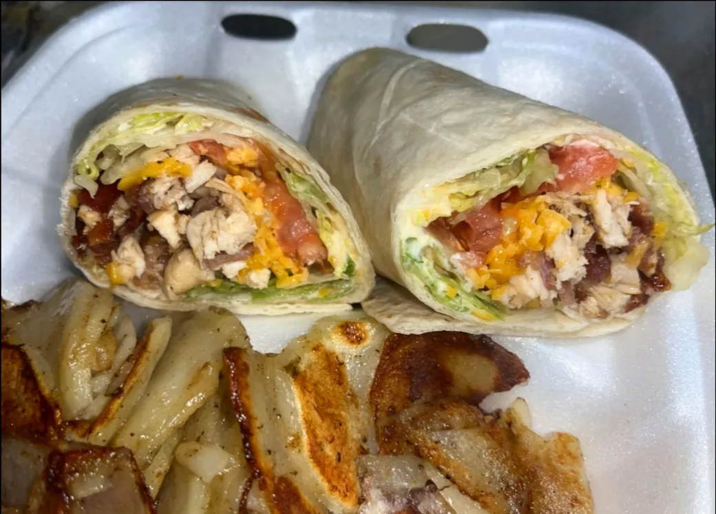Chicken bacon ranch wrap cut in half with lettuce, tomato and cheddar, served with fried potatoes