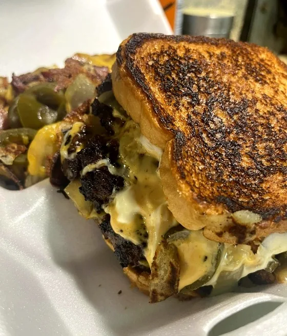 Patty melt on griddled toast with melted cheese and pickles